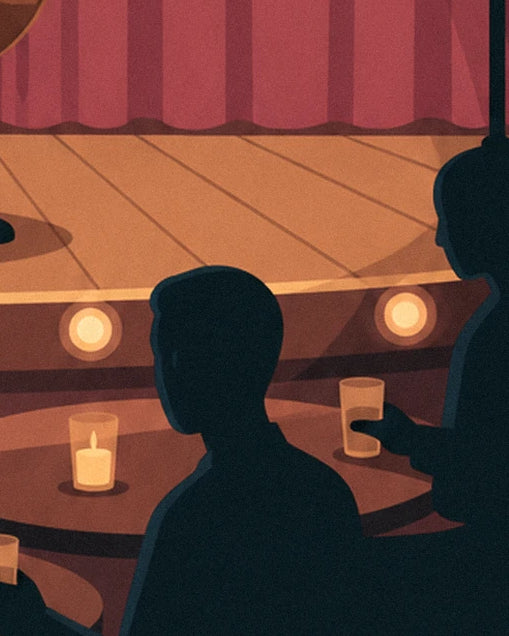 Audience members in silhouette, glasses in hand, in front of the lights along the edge of the stage