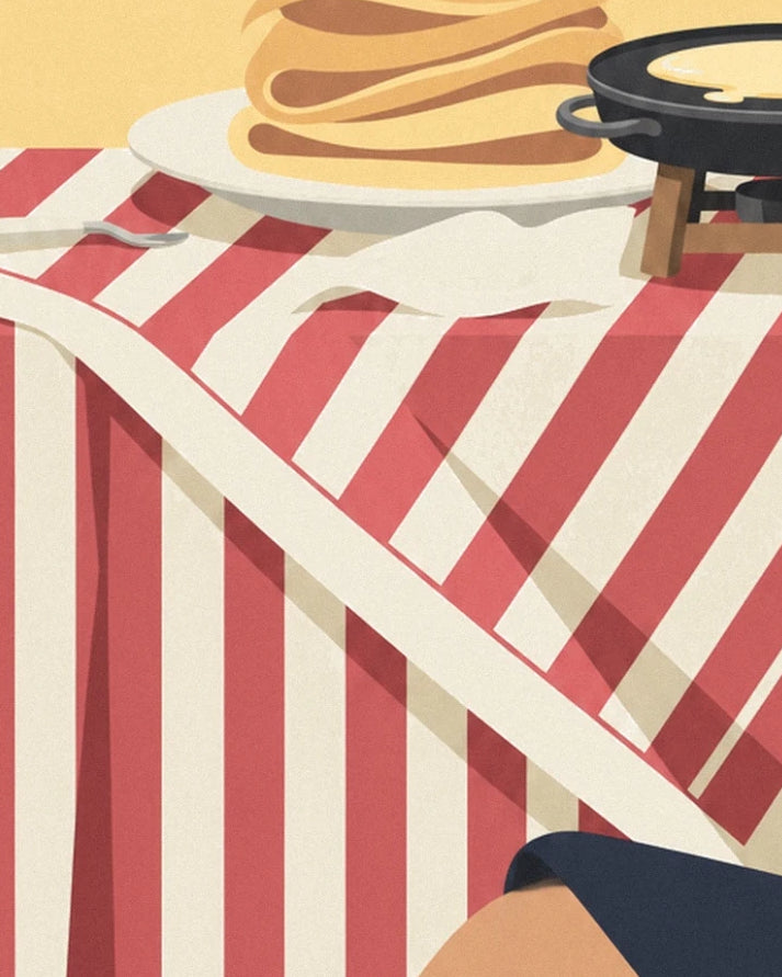 The red and cream striped tablecloth beneath the plate of crêpes and the crêpe pan