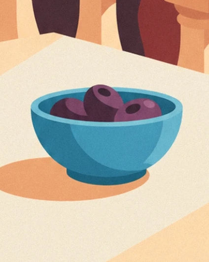 Un bol bleu rempli d’olives violettes sur une table claire ensoleillée